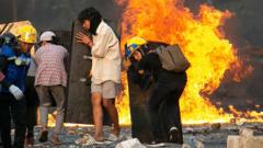 Protestors behind shields on burning street in Myanmar.