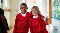 Two boys stand in a school corridor. One has their arm around the other's shoulders. They are wearing white polo shirts and red jumpers.