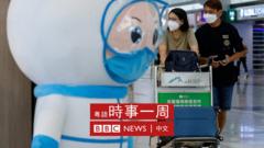 香港国际机场客运大楼内宣传新冠防疫的巨型娃娃摆设与戴着口罩的旅客（1/8/2022）