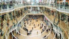 Fotografia colorida mostra pessoas em um shopping e números brancos tipo matriz flutuando em todo o ambiente