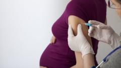 Enfermeira aplica vacina no braço de grávida; ambas estão de lado para a câmera