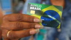 Mão feminina segurando cartão do Auxílio Brasil ilustrado com a bandeira nacional