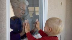 A baby visits an elderly neighbour though a glass window