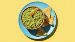 A blue plate with tortilla chips and a bowl of guacamole on a yellow background