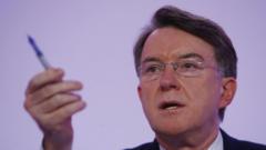 Lord Mandelson, wearing glasses, holds a pen.