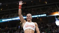 Cringle waiving to the crowd in the arena. She is wearing a white vest with leader on the front in red lettering and her name beneath it.