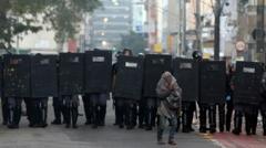 Homem se protegendo na frente de barreira de policiais com escudos, na Cracolândia