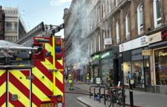 Smoke pours out of several windows and doors of a Victorian building on Union Street Glasgow in a photo taken at 1606 on Sunday 8 March. There is a fire appliance in the foreground and three firefighters can bee seen in the street.