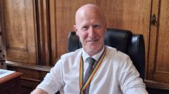 Lee Ratcliffe is wearing a white shirt with the sleeves rolled up and a blue and white patterned tie