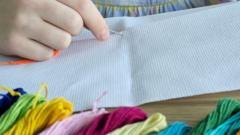 A child's hand holding a needle with coloured embroidery threads at the foreground