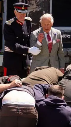 King Charles has arm held by uniformed officer as men scramble in a scrum in front of him