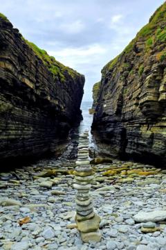 Stones stacked into a tall tower on a rocky shore with the sea and cliffs behind.