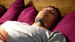 A man asleep in bed with a black boomerang-shaped device attached to his neck.