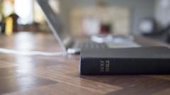 Bíblia em cima da mesa, com laptop atrás