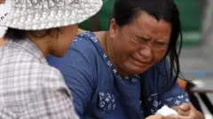A woman in a blue shirt with a distraught expression is comforted as she cries.