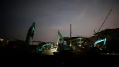 Excavators working through the rubble at night