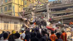 A large group of rescue personnel in front of a collapse building, several are on top of some rubble.