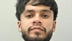 A mugshot of a young man with a short beard and dark hair.