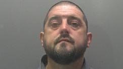 The image police took of Alfred Stanley in custody. He has a buzzcut and a dark beard and moustache.