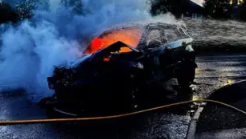 The Range Rover is engulfed in flames with smoke billowing from the vehicle. It is parked in a street at dusk.