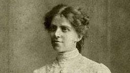 A faded black and white picture of a woman wearing a high necked white shirt and with her hair up. She is dressed in Edwardian style.