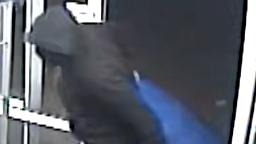 Photo from shop CCTV showing a robbery suspect. The photo is blurry but shows the suspect in dark clothing carrying a large blue bag