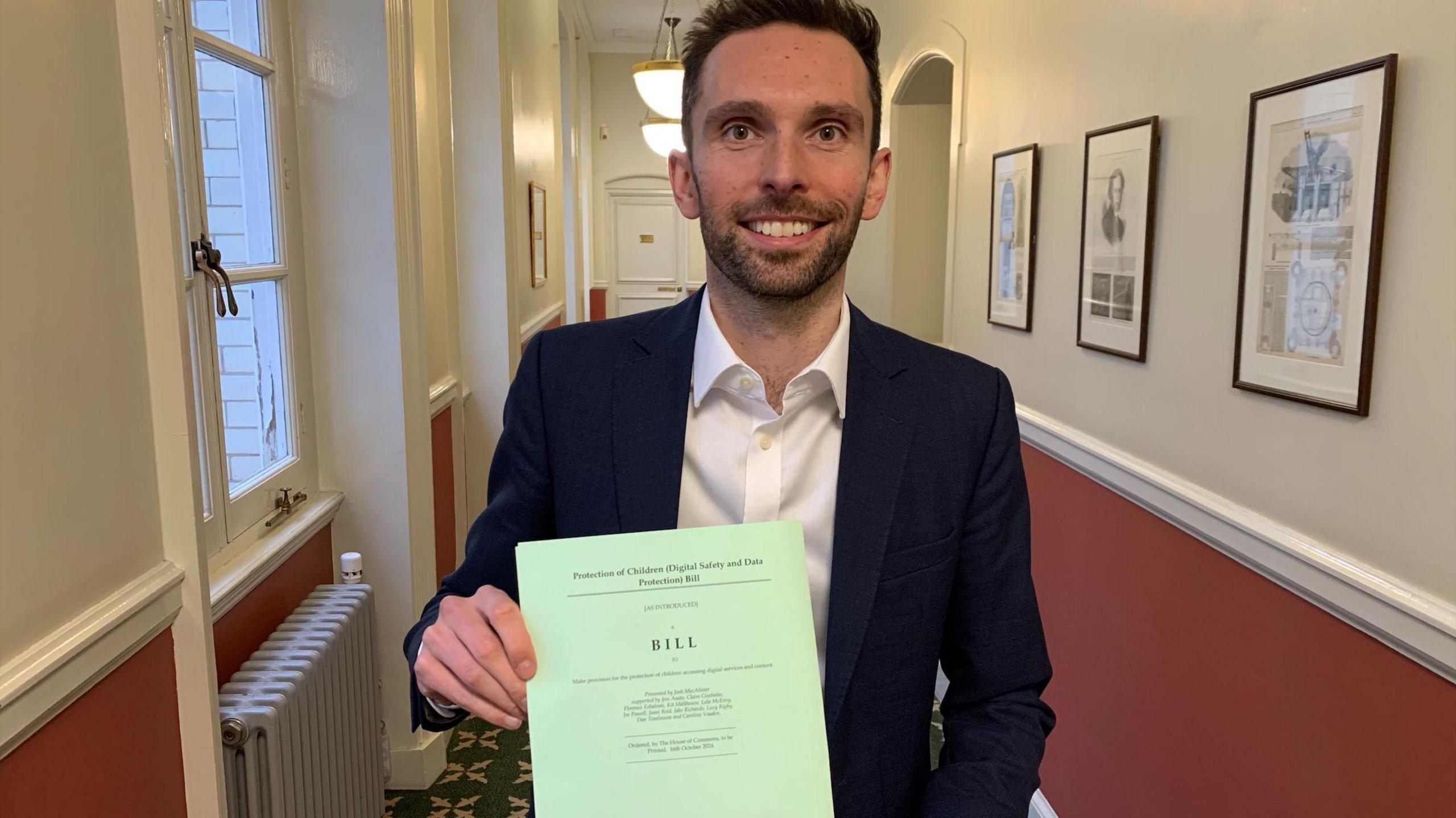 MP Josh MacAlister holding up a copy of the draft bill