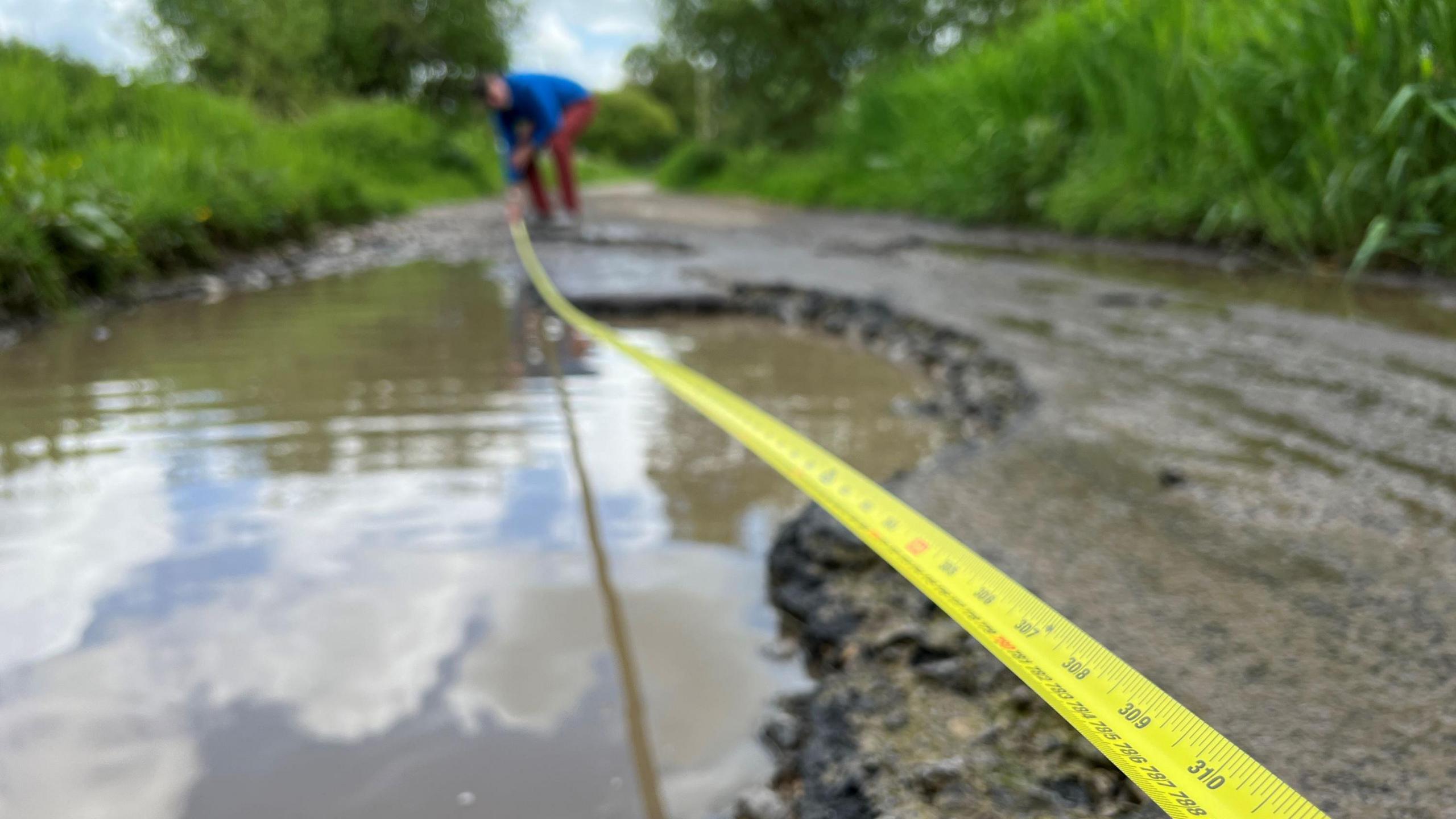 A tape measure being held across the pothole which is full of water