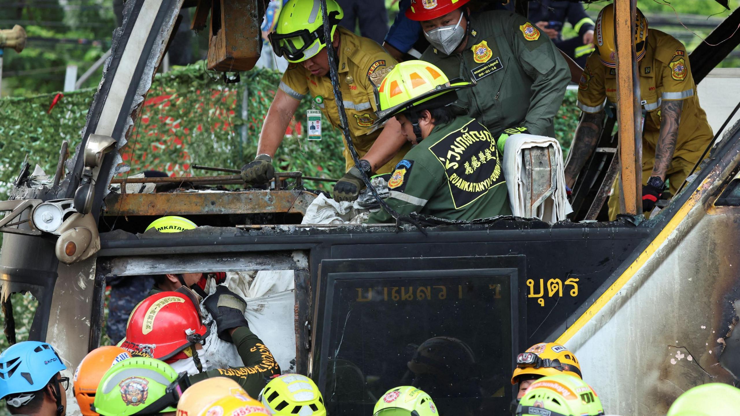 Firefighters transfer bodies from a burnt-out bus that was carrying teachers and students from Wat Khao Phraya school, 