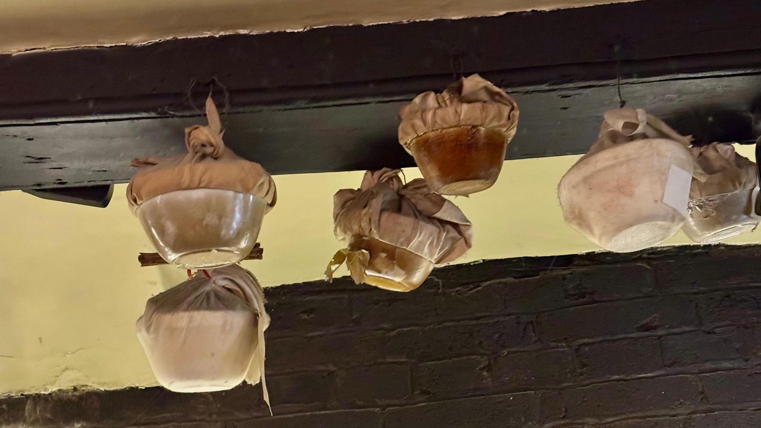 Christmas puddings in bowls and wrapped in fabric hang from the beams of an old pub. 