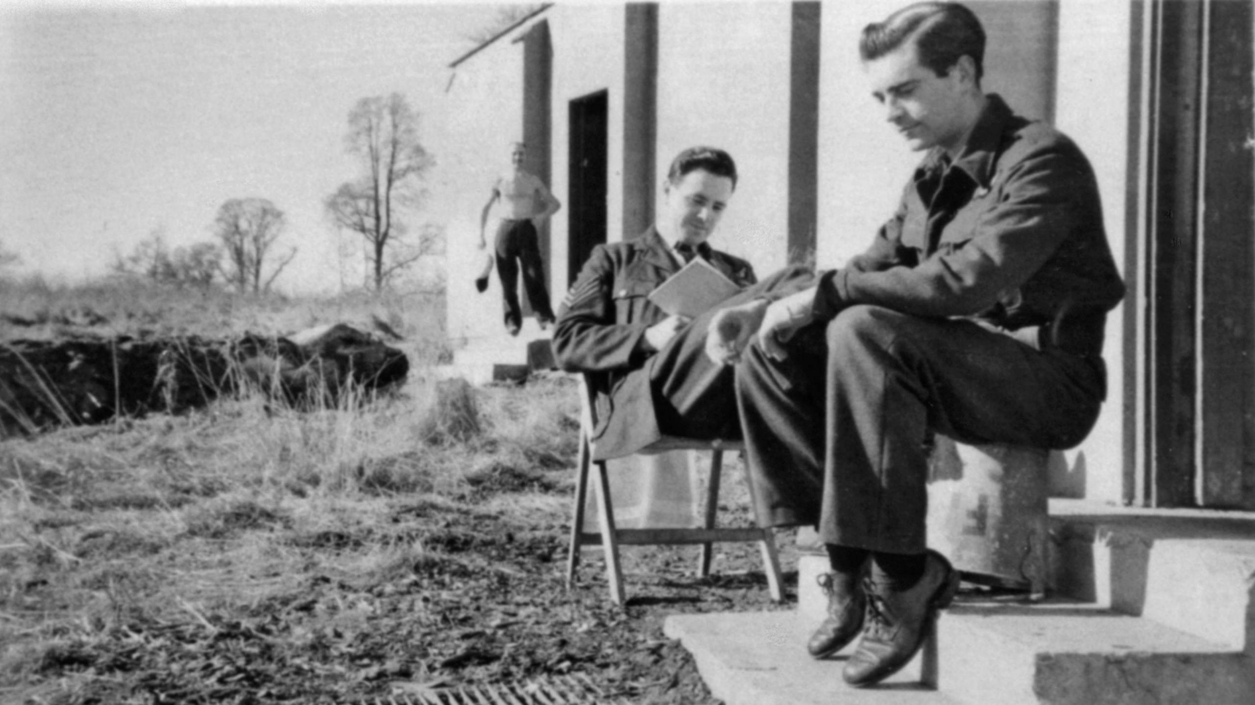 A black and white archived photograph of an airmen's billet at Croome Court shows personnel sitting outside their accomodation in the sunshine. One of them is reading.