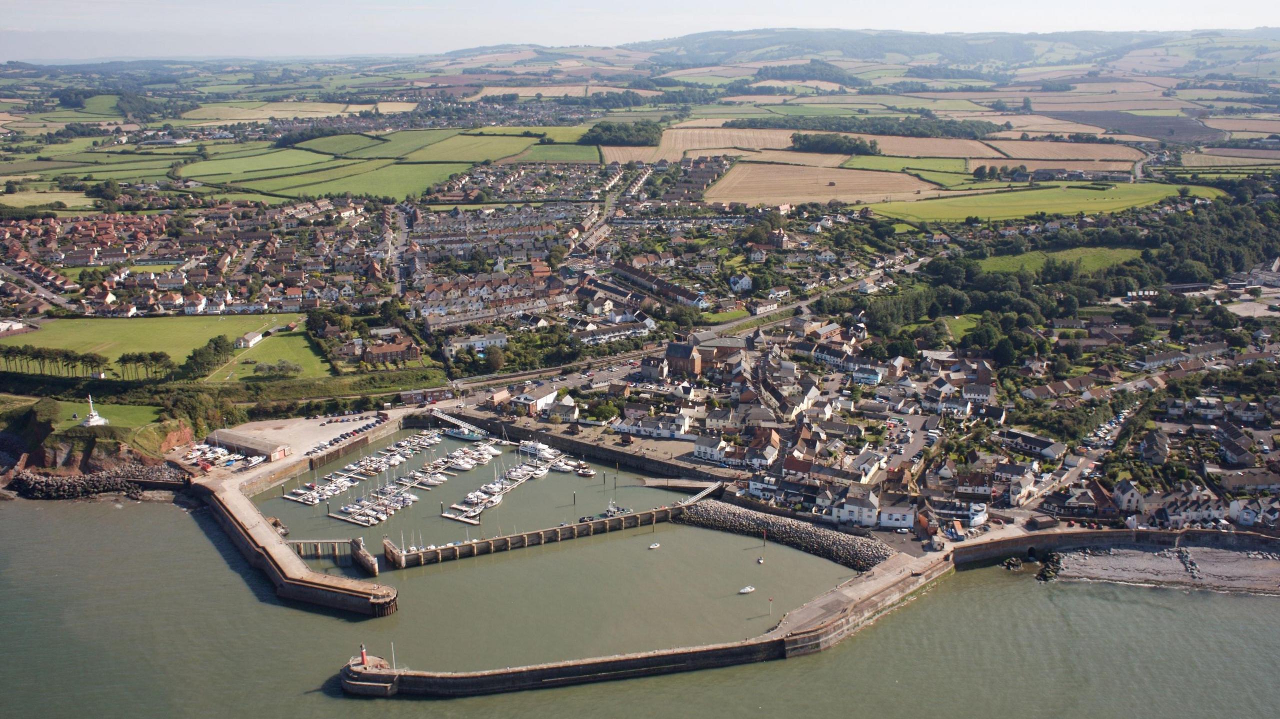 An aerial view of Watchet Harbour in west Somerset. The walls of the harbour are visible, and the town spreads out behind it. Boats can by seen in the harbour.