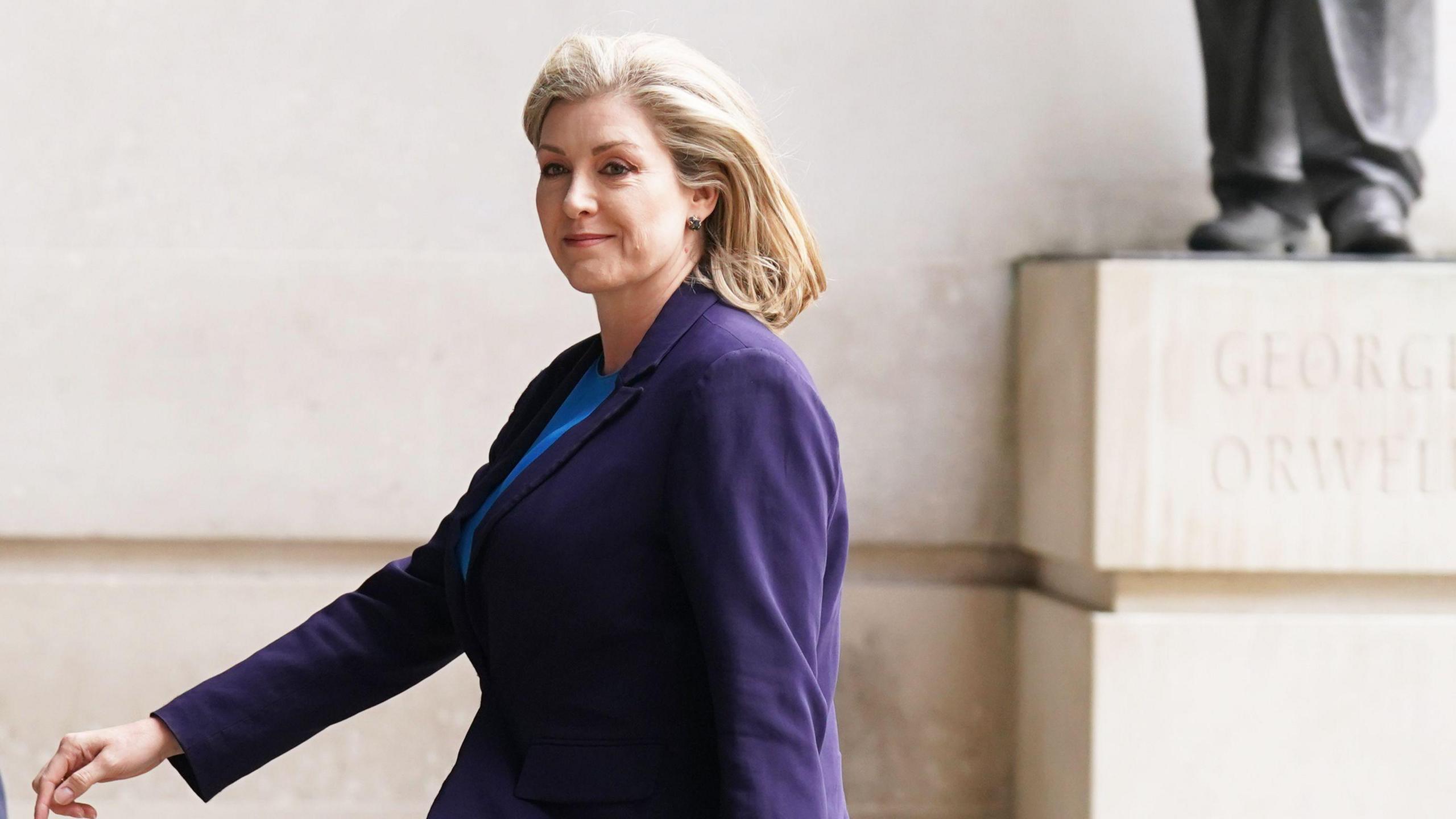 Penny Mordaunt with a blow-dry wearing a purple jacket walking near to New Broadcasting House