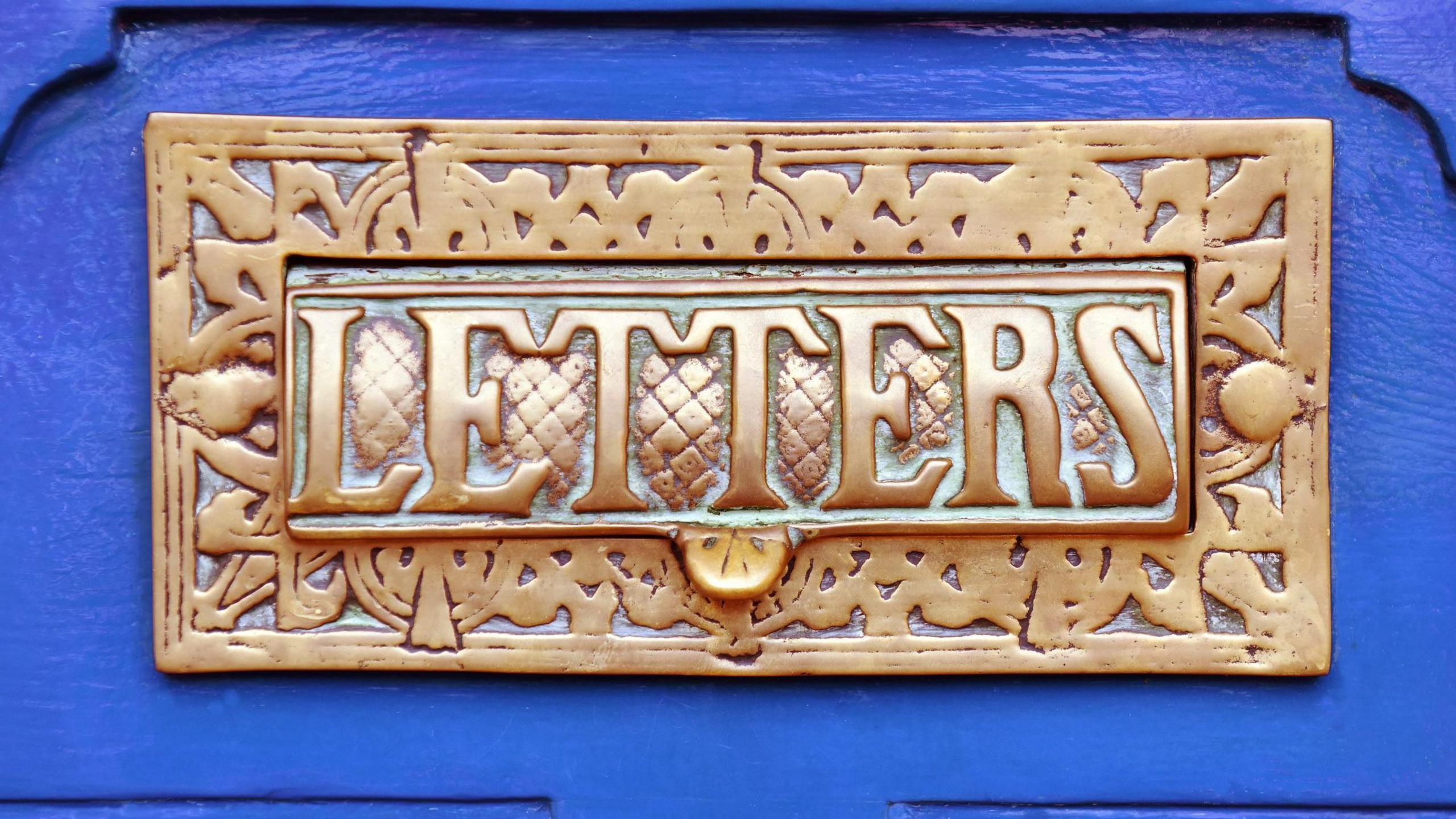 An ornate brass letterbox in a bright blue painted door