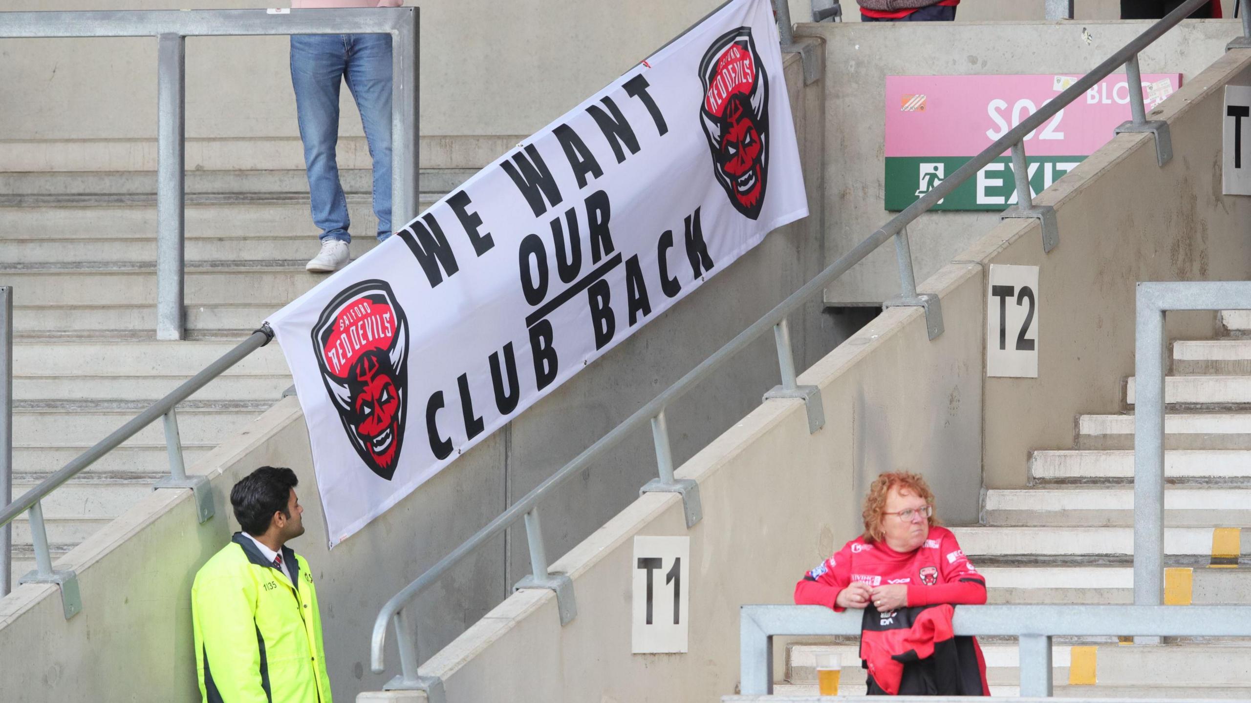 A Salford Red Devils banner displaying the message "we want our club back" at a Super League fixture against Wigan Warriors this season