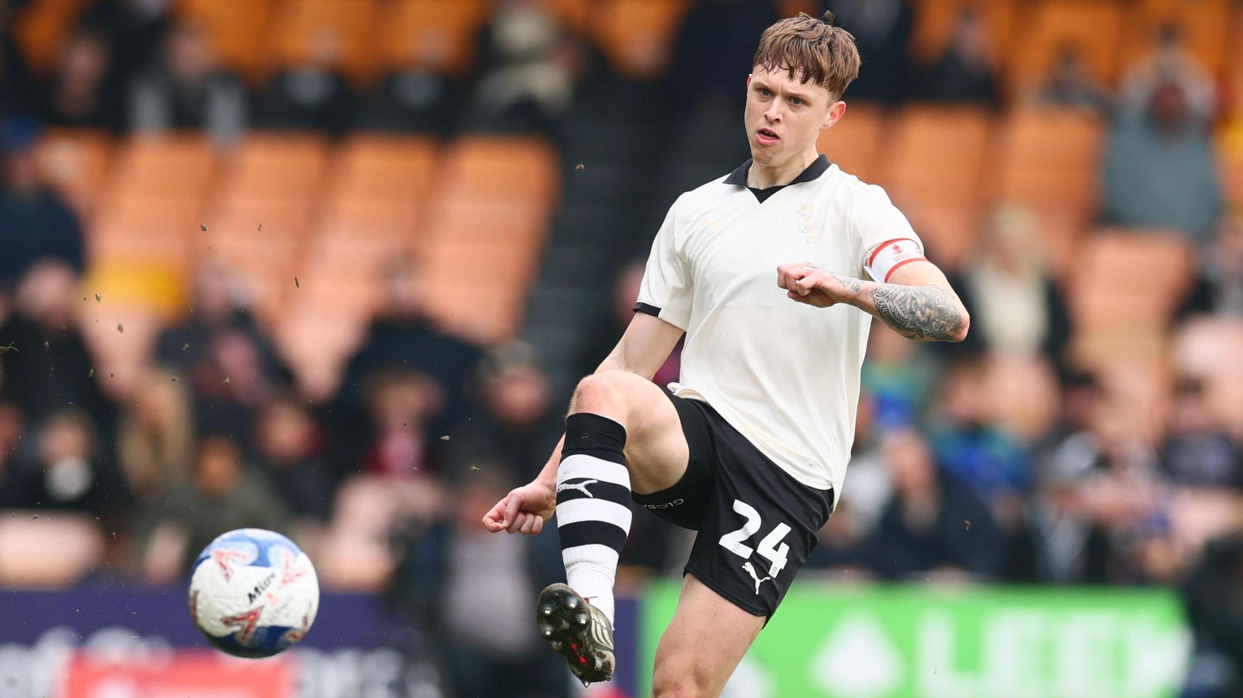 Kyle John aims a pass forward with his right foot during a game for Port Vale. He is wearing a white shirt, black socks and black-and-white hooped socks.