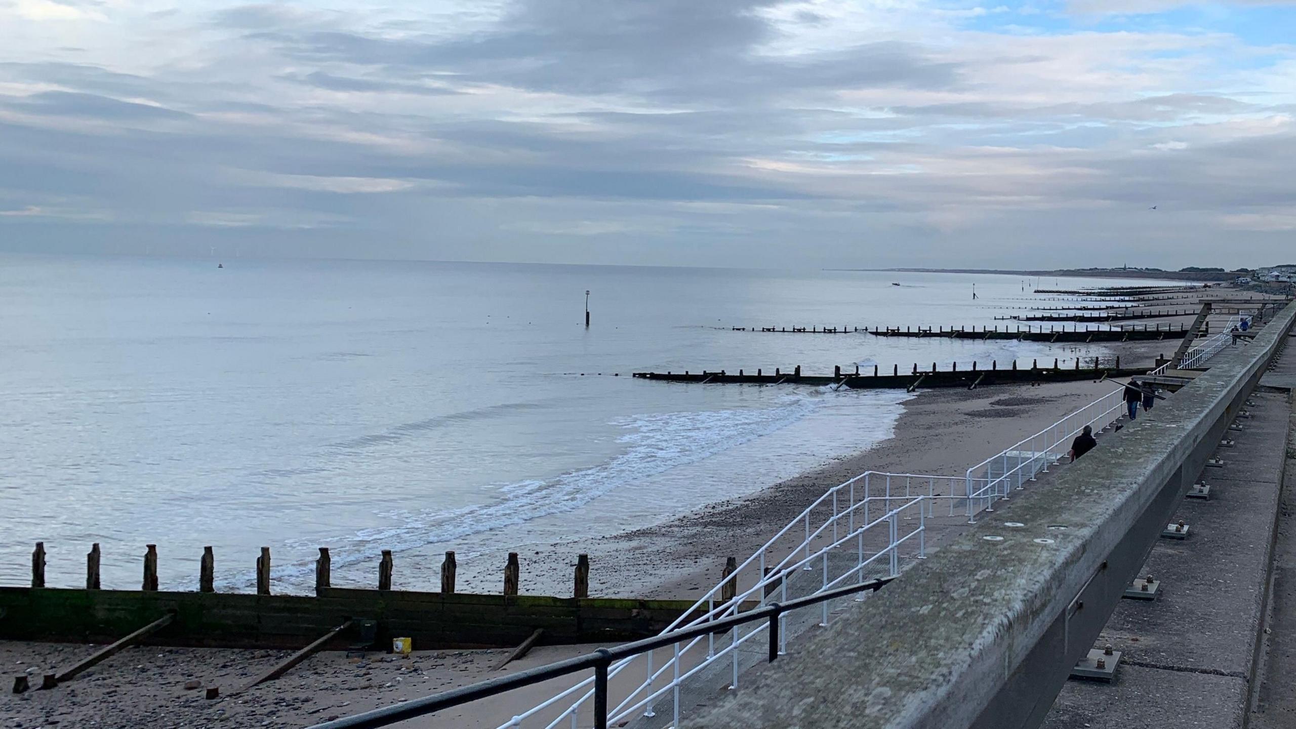 Landscape view of Hornsea beach from the promenade with sea water lapping against a row of groynes