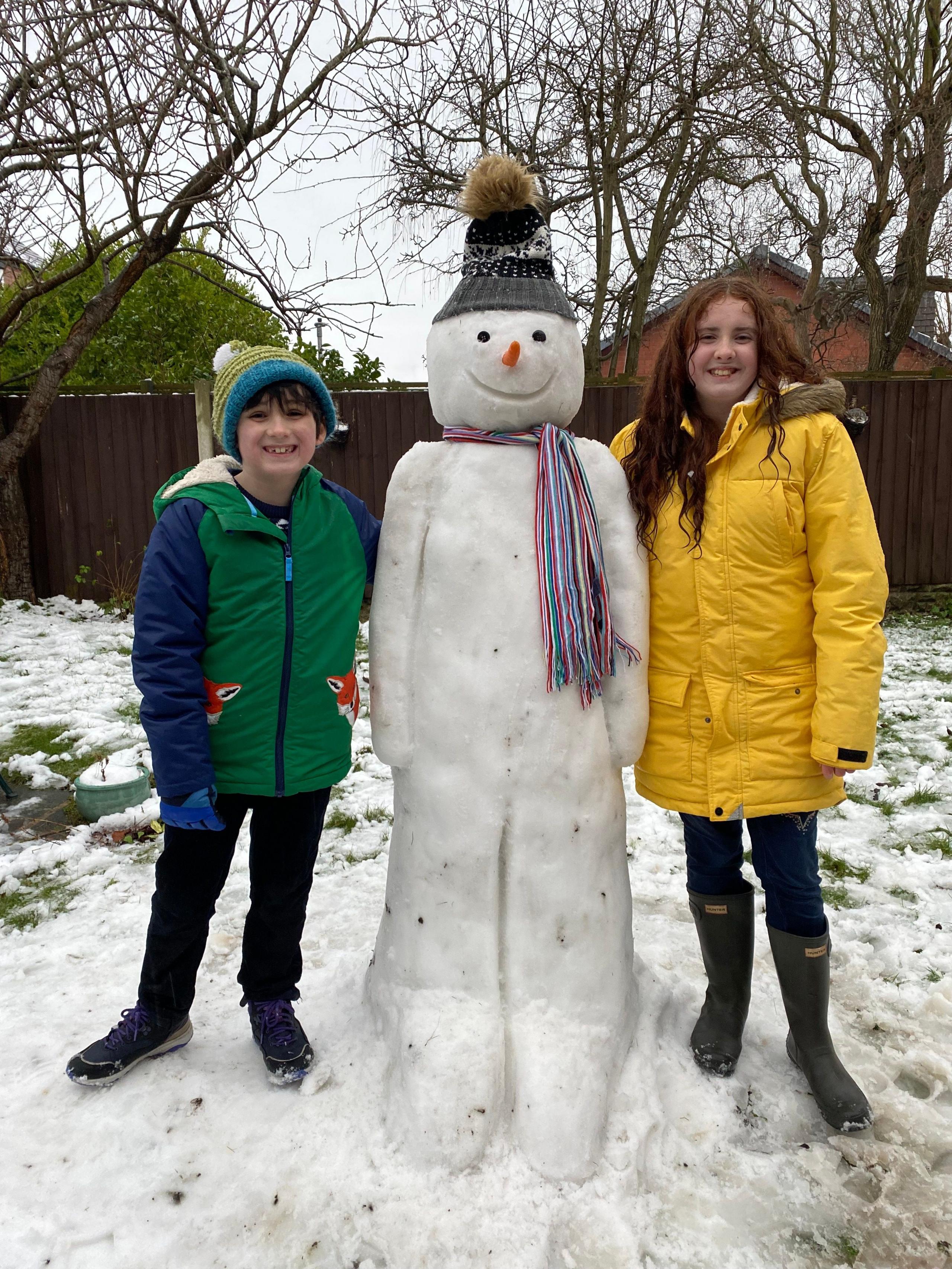 Two children stand next to thier impressive snowman.