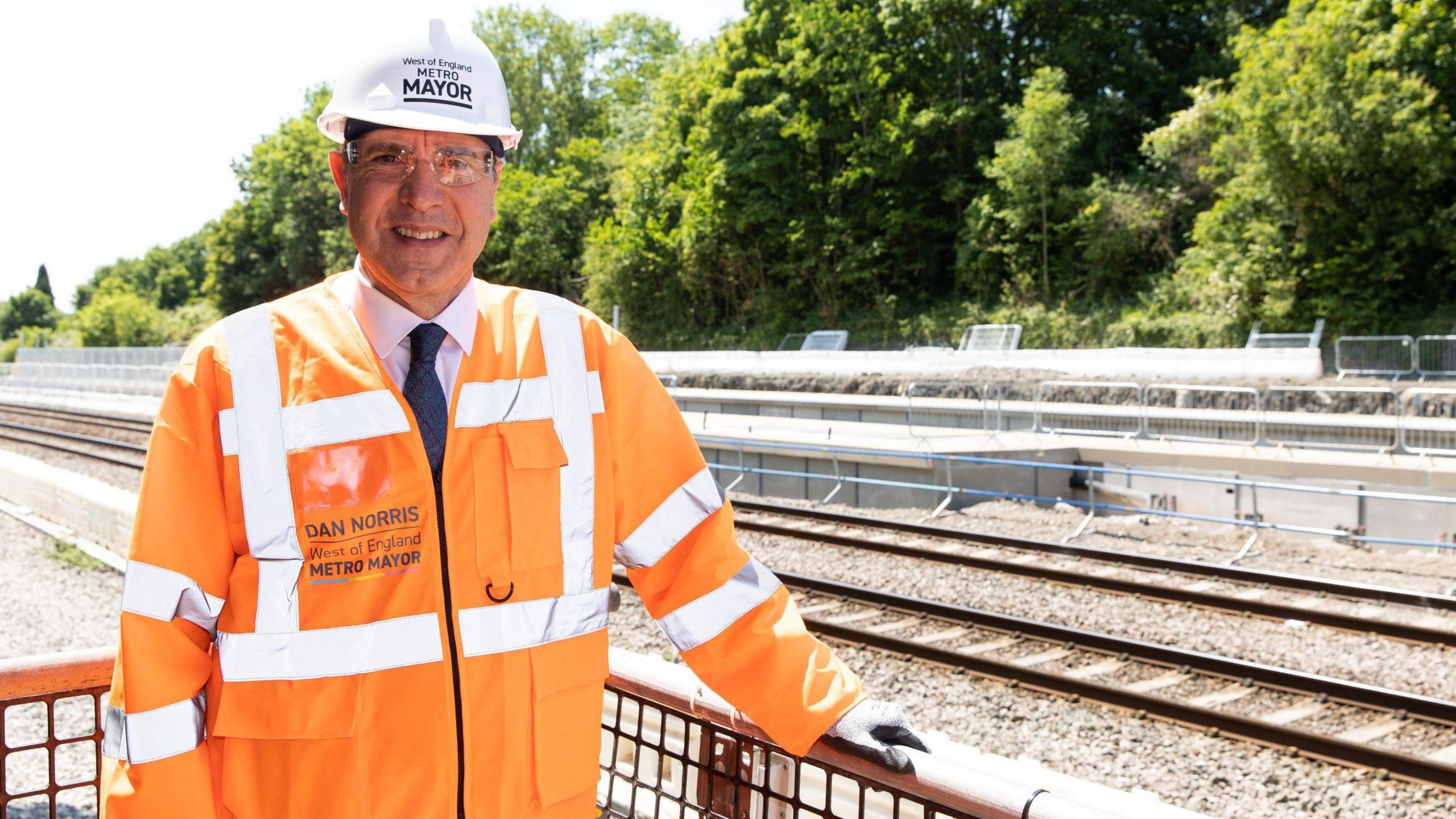 West of England Mayor is pictured in an orange hi-vis jacket and hard hat, next to the railway line at Ashley Down.