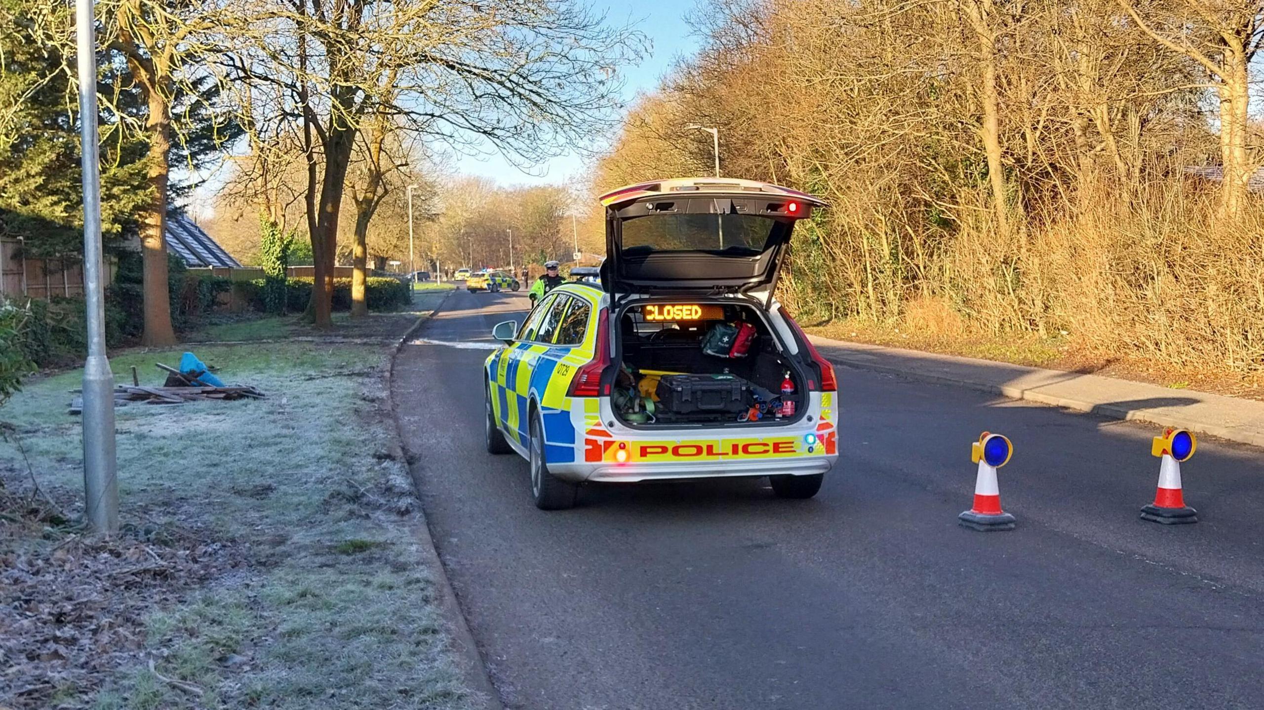 A police cordon on a road. There is a hard frost shown on one side of the road