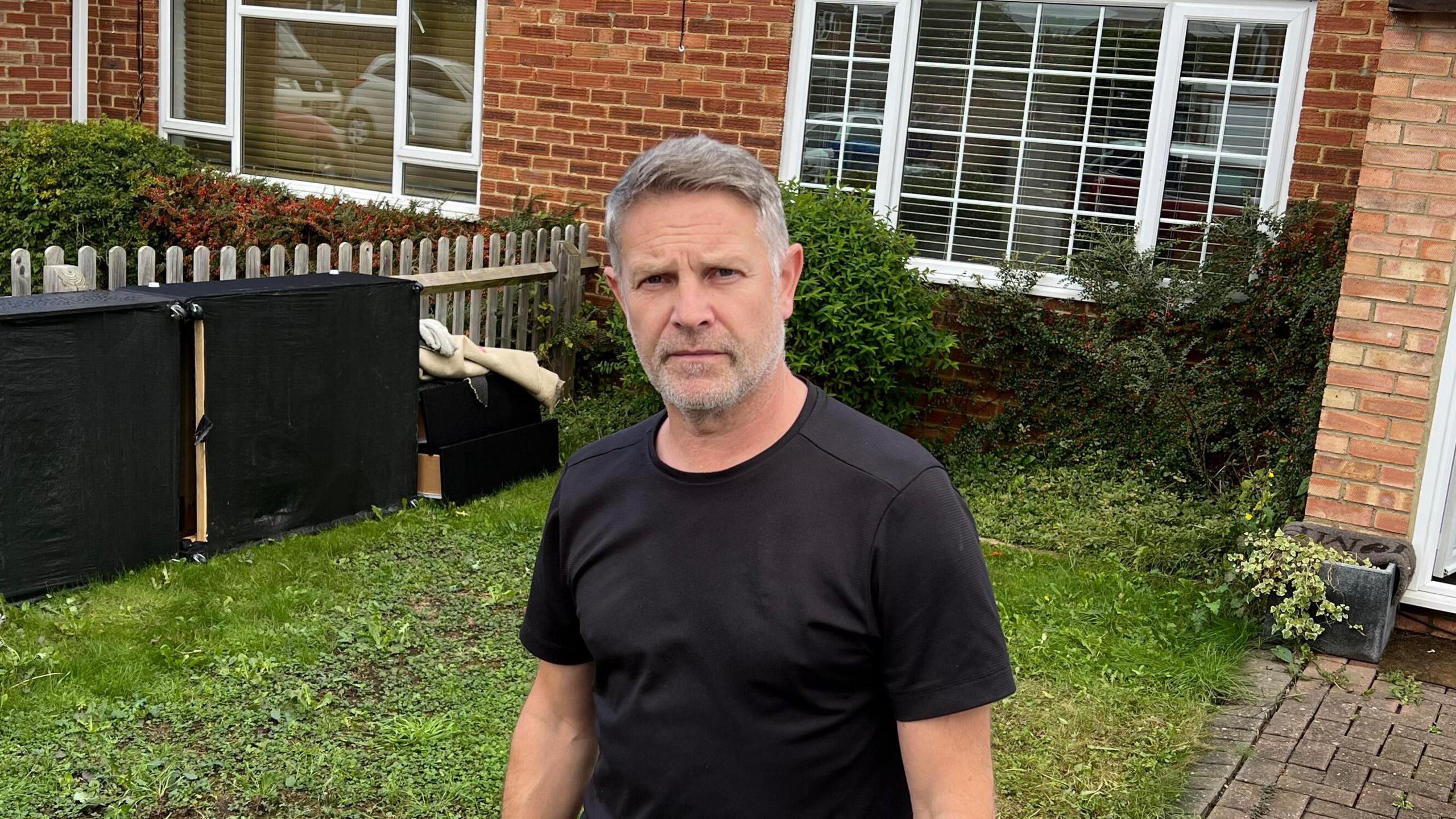 Darren Butler stood outside of his home. He is wearing a black t-shirt.