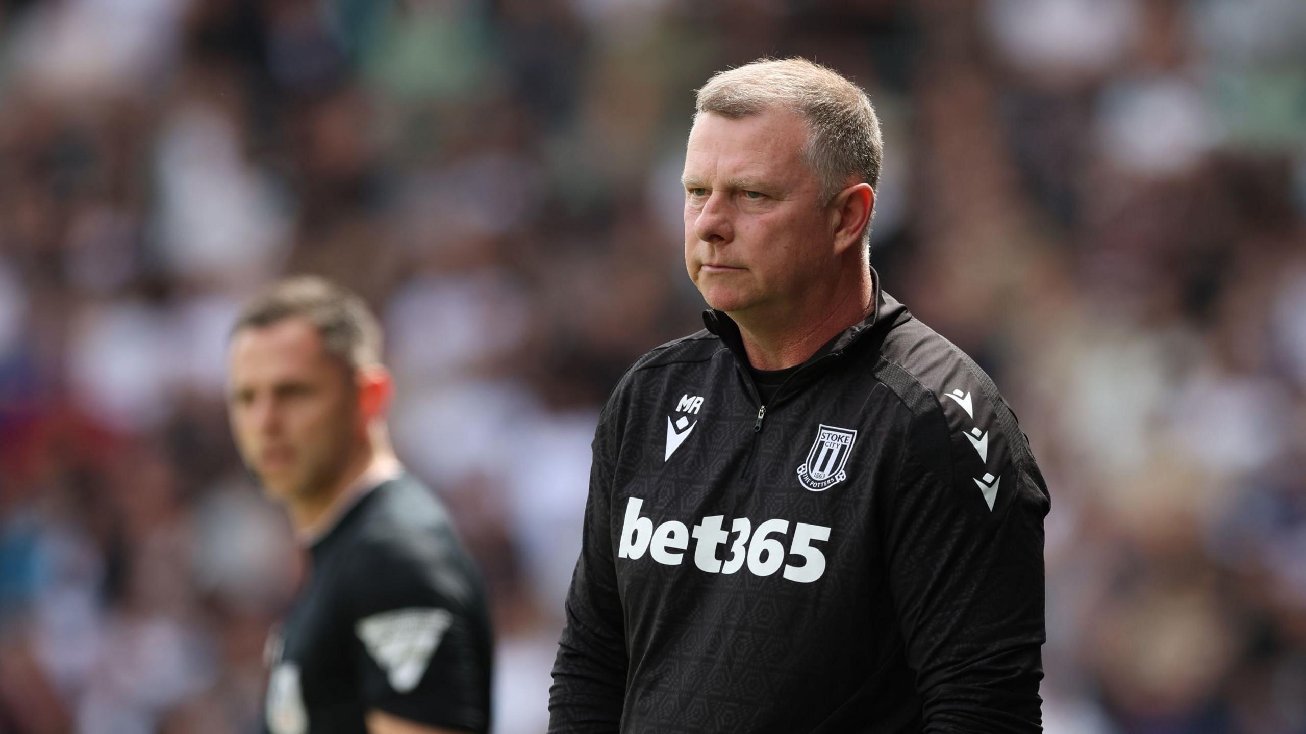 Mark Robins in his black Stoke City training top looks on from the touchline during a game