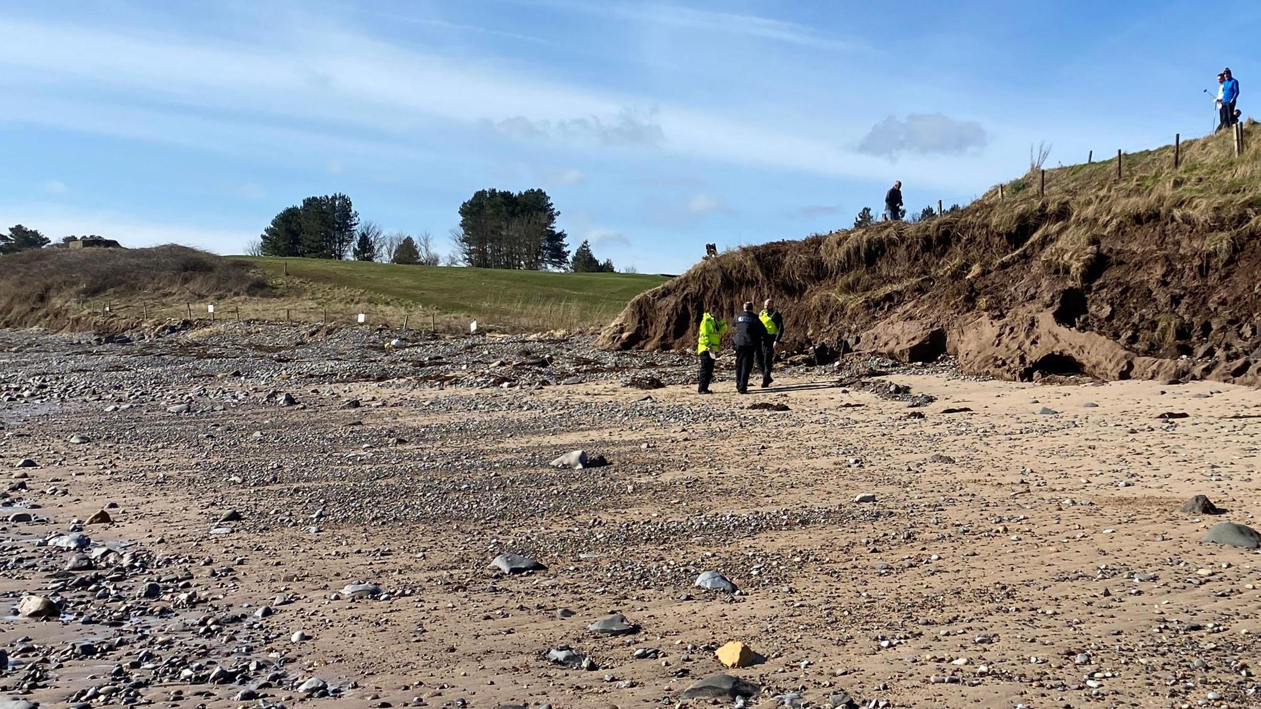 A number of police officers inspecting the base of a muddy cliff 