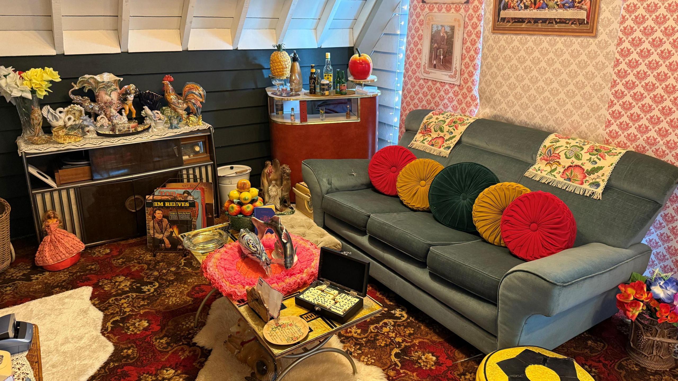 A colourful front room with a sofa and coffee table, covered in ornaments.