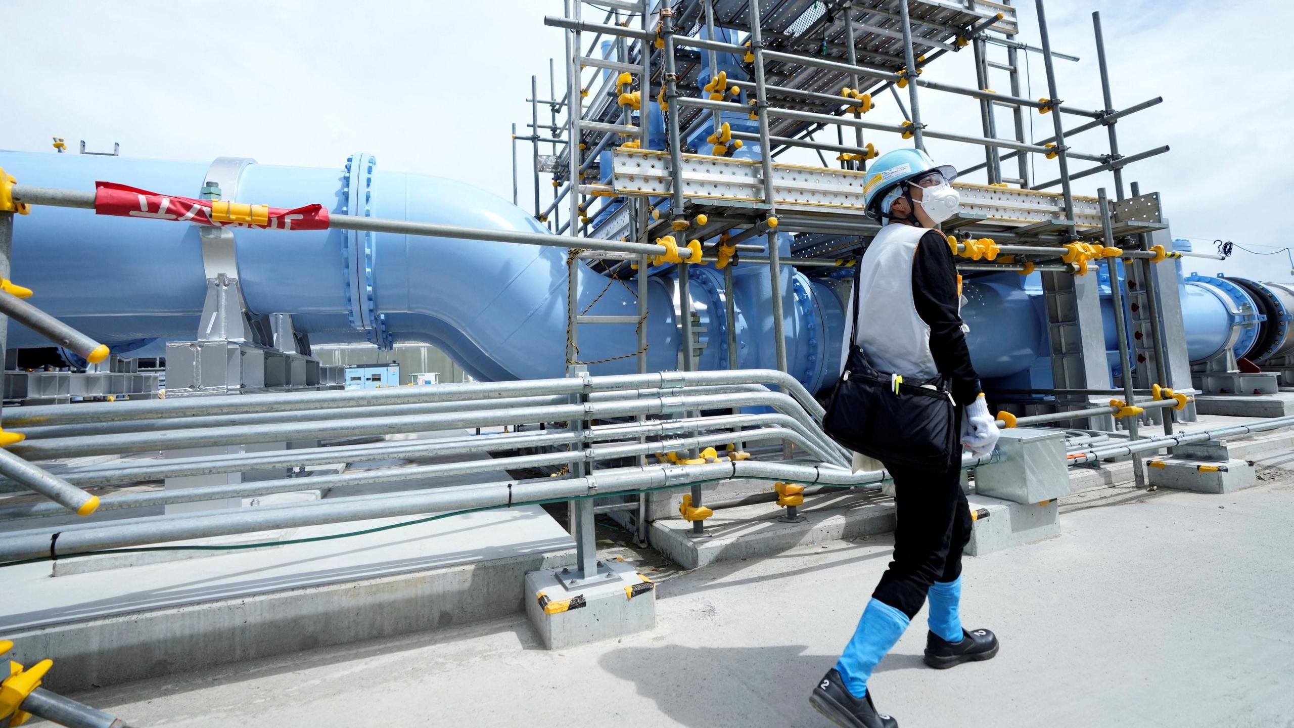 Man walks past a pipeline at the Fukushima Daiichi nuclear power plant