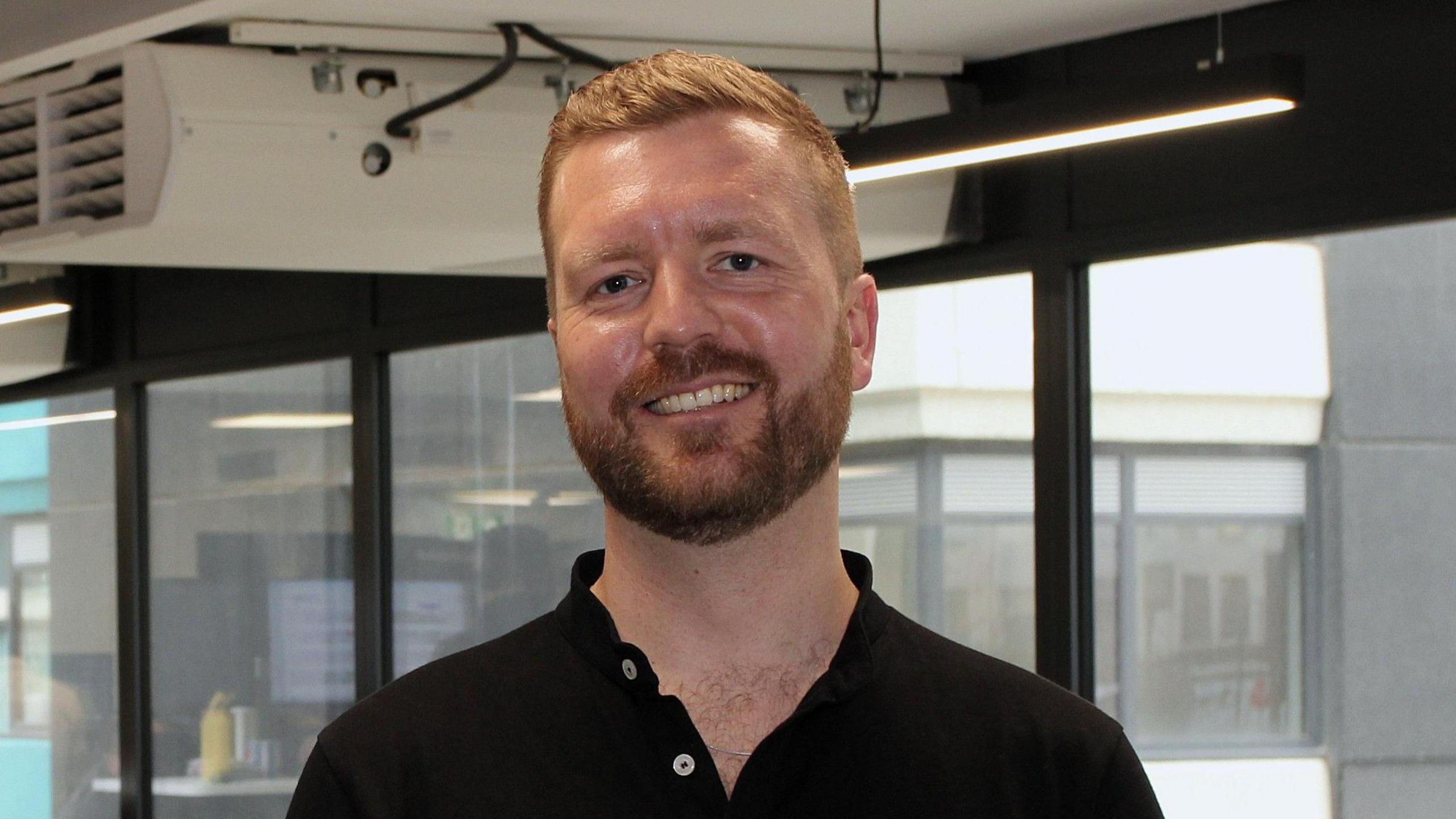A smiling Chris Iveson wearing a black polo shirt looks straight into the camera.