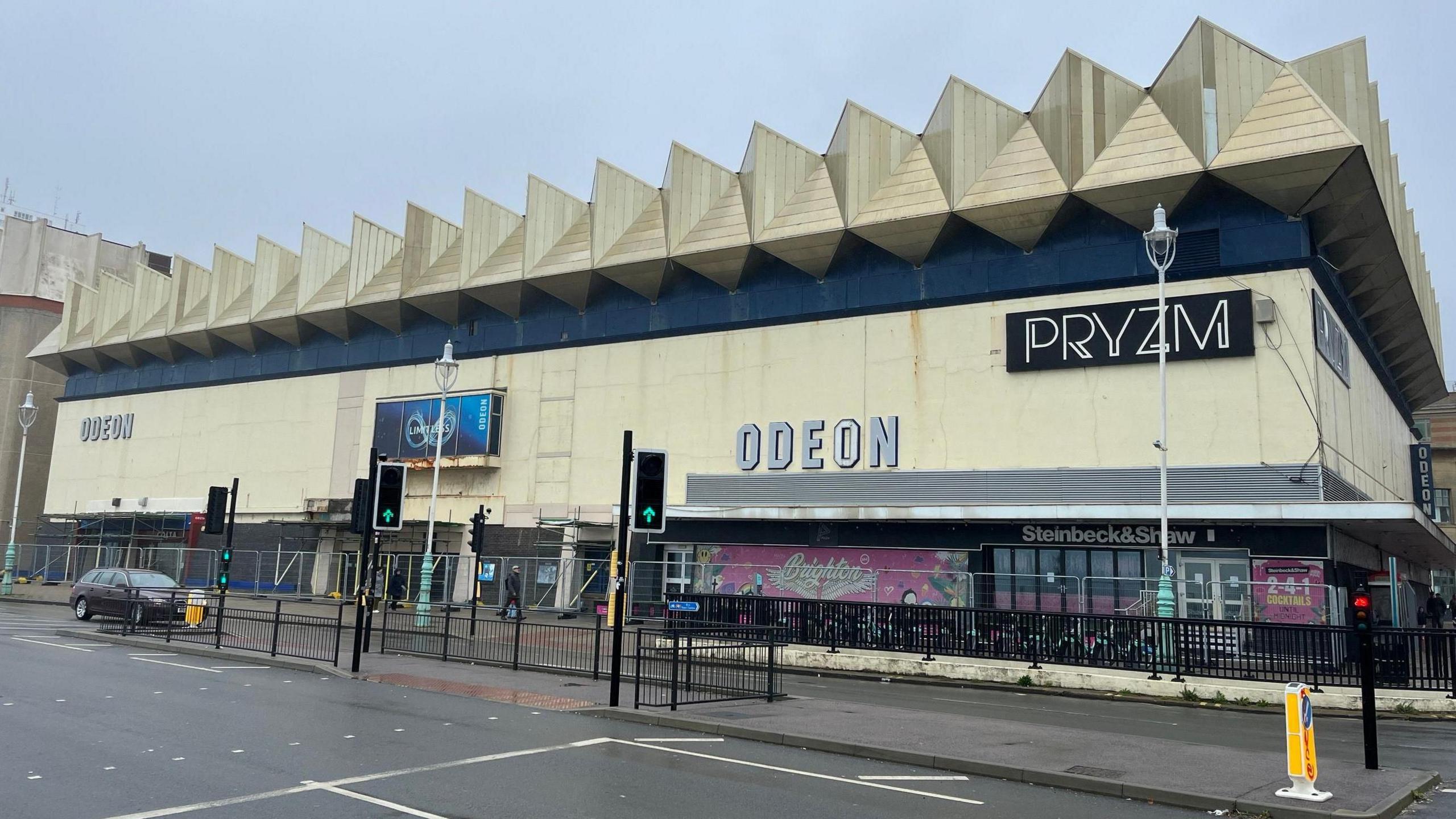 A large beige building with a spiky roof, with signs for Odeon and Pryzm on the front.