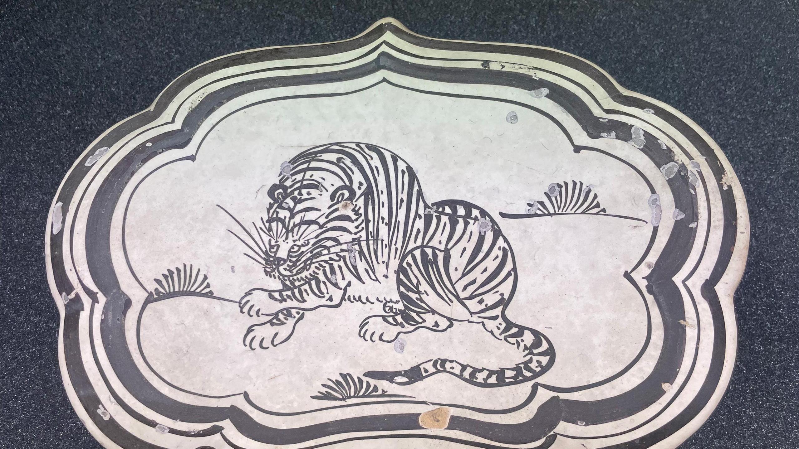 A ceramic pillow which features a white base with the black depiction of a tiger skulking in grass.
