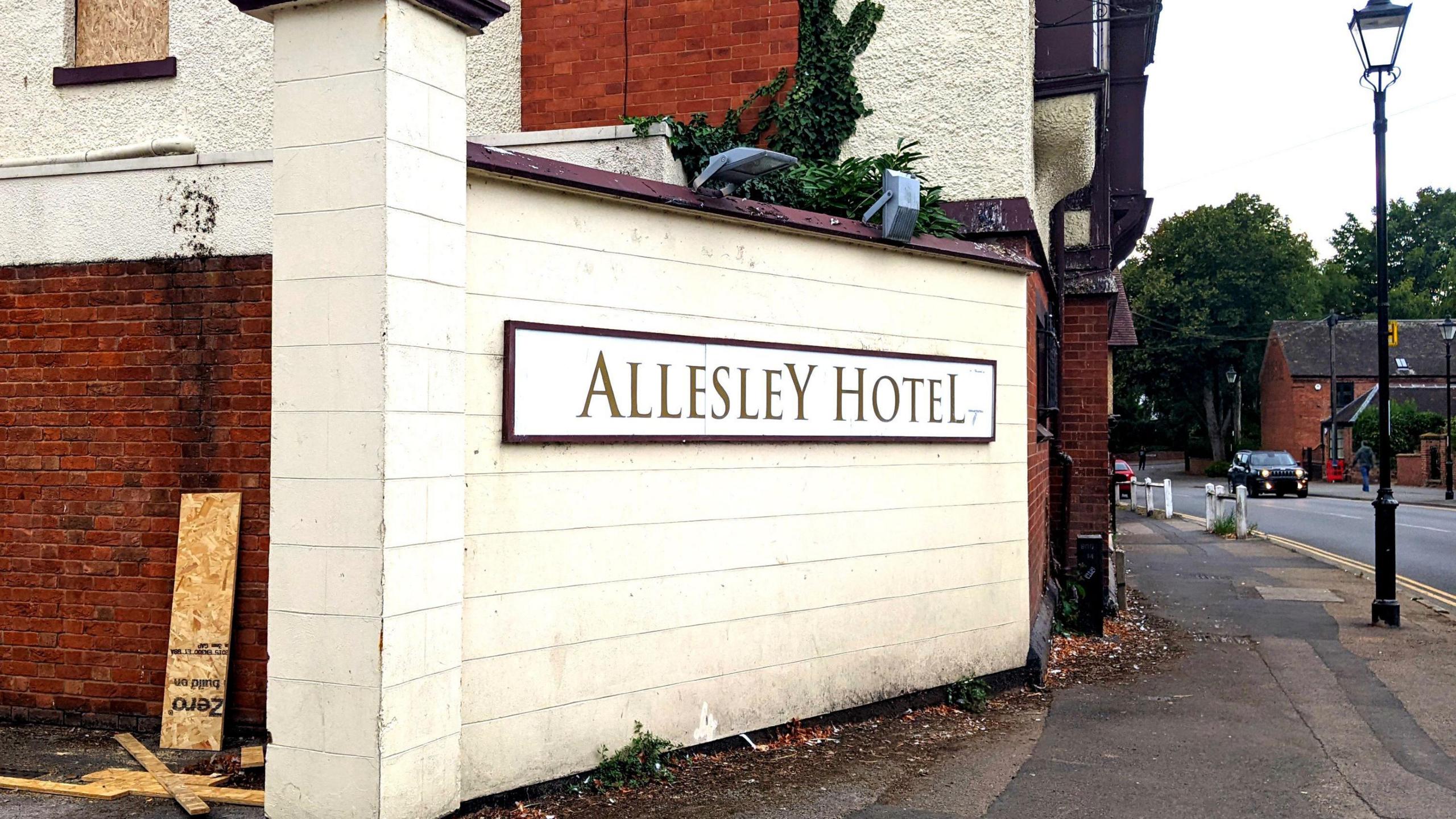 A cream and maroon sign saying "Allesley Hotel" is on a wall outside the premises. A road runs alongside.