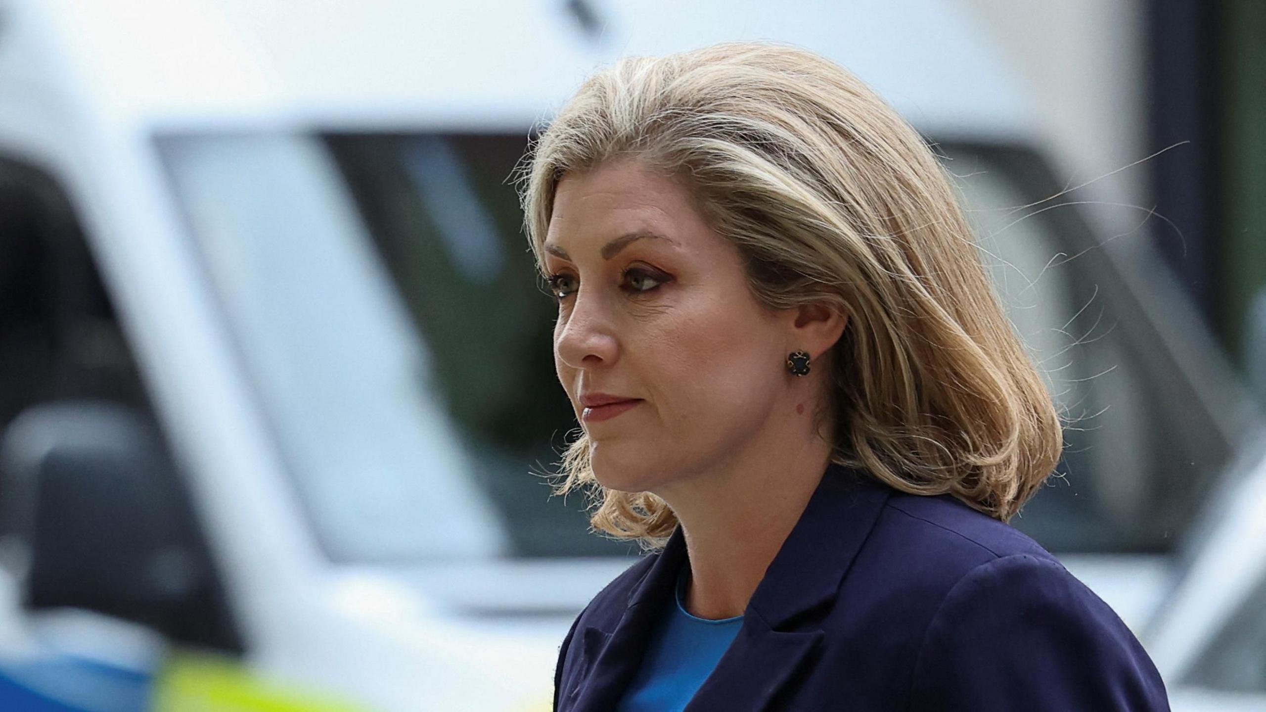 Penny Mordaunt is pictured walking outdoors. She wears a dark suit.